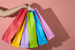 © Answer 7 - Male hand holding many multicolored shopping bags on a pink background, shopping concept