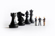 © Yunus Nugraha - Miniature people standing next to chess pieces on a white background. Businessman discuss strategic steps.