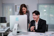 © amnaj - Two asian businesspeople discussing work and analyzing financial charts using desktop computer in modern office, smiling and enjoying their work