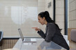 © amnaj - Asian businesswoman is pointing at her laptop and laughing while making a video call in a modern office environment, enjoying a moment of amusement during her workday