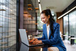 © amnaj - Smiling businesswoman using laptop and enjoying a matcha latte in a modern office cafe, showcasing a productive and enjoyable work environment
