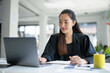 © amnaj - Young Asian businesswoman wearing black suit using laptop computer working at modern office, smiling female executive manager typing on keyboard at workplace