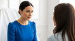 © mumtaz - Professional woman in blue blouse having a serious conversation with a female patient in a clinical setting during a consultation or therapy session in a modern medical office environment
