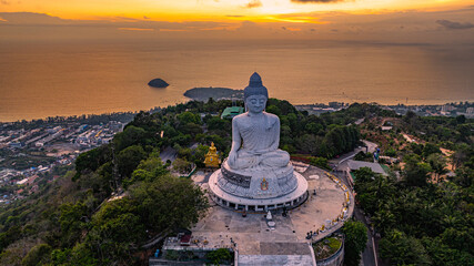 Wall Mural - A breathtaking aerial view of the iconic Big Buddha statue overlooking the Andaman Sea in Phuket, Thailand, captured during a vibrant sunset. The golden sky reflects on the water, majestic hilltop