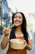 © Westend61 - Happy person eating fresh salad outdoors in urban street