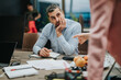 © qunica.com - Businessman seated while attentively listening during an office interaction, reflecting on a subject with apparent concern and focus. The environment is professional, showcasing a modern workspace.
