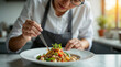 © dubogray1985 - Close-up of a female chef in a clean modern kitchen plating a gourmet dish with tweezers