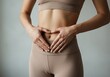 © Senja - A fit woman in beige activewear makes a heart shape with her hands on her flat stomach, symbolizing gut health, digestive wellness, and self-care.