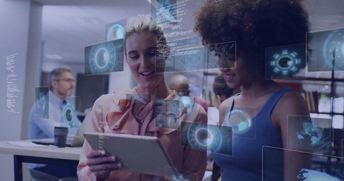 Examining female colleagues discussing tablet in open office, with floating holographic charts