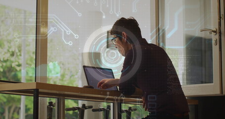 Leaning man in collared shirt using laptop at office standing desk with digital overlay, copy space