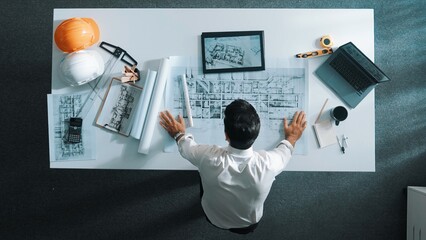 Poster - Top down view of skilled engineer talking to manager by using mobile phone while raised hand to celebrate successful project at meeting table with safety helmet, laptop and equipment. Alimentation.