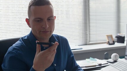Wall Mural - Medium shot of focused adult male manager picking up smartphone from desk phone holder recording voice message while communicating with business colleagues during working day at modern office