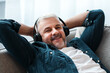 © Prostock-studio - Happy matured man reclining on couch at home, listening to music and smiling, using wireless modern headset, closeup, copy space. Modern technologies and entertainment concept