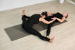 © TRAVELARIUM - Two young women in calm studio engage in partner yoga. They stretch on gray mat, fostering flexibility and relaxation. Neutral tones enhance serene ambiance
