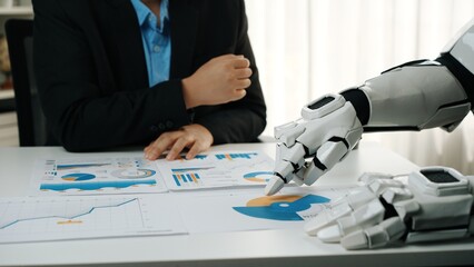Poster - A modern office scene featuring a human and a robotic hand collaborating on data analysis. Focus on reports with graphs and charts highlighting business insights.Noogenesis