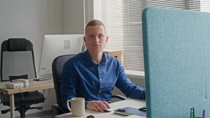 Wall Mural - Portrait of adult male office worker wearing blue shirt confidently turning to camera while using computer working at desk in contemporary workspace, slow motion