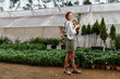 © SHOTPRIME STUDIO - Young woman in a greenhouse holding plants, wearing a white blouse and green skirt, enjoying nature with greenery in the background and warm earthy tones