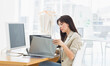 © WavebreakMediaMicro - Woman working on laptop with external monitor and clothes rack behind while sitting at office desk
