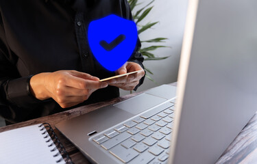 Poster - Businesswoman holding a credit card in front of a computer and a shield icon, safe online shopping concept