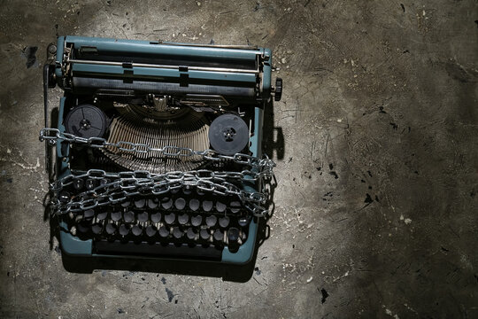 Vintage typewriter with chains on grey grunge background. Printing ban concept