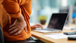 © AdamDiezel - Man sitting at his desk and experiencing back pain due to poor posture while working in the office, holding his lower spine with hand.