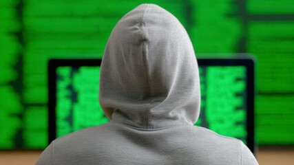 Poster - Digital Vigilance: A person in a hoodie is focused on a laptop. Behind, a display of green code underscores the themes of technology and data security.