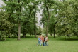 © AnnaStills - Group of multiethnic children walking with Caucasian female teacher through green park, kids carrying backpacks, teacher leading students outdoors, trees and grass surrounding group