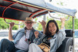 © bongkarn - Couple of old white man and asian woman sitting riding in tuk tuk three wheeled taxi touring a city.
