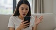 © Atelier d’Alya - Shocked Asian woman reacts to phone content at home on sofa