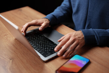 Poster - Hands typing on a laptop keyboard with a smartphone resting on a wooden desk during the evening