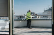 © qunica.com - Two construction engineers wearing safety vests and helmets discuss building plans on a rooftop, with a cityscape in the background. They appear focused on the progress of the project.