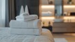 © Iaroslav - Freshly laundered white towels are neatly stacked on a bed, ready for guests in a modern, clean hotel room