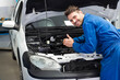 © WavebreakMediaMicro - Male mechanic in garage leaning into car engine under open hood showing support rod, copy space