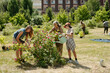 © pressmaster - Multiethnic group including senior Caucasian woman, teenage Caucasian girl and teenage Black boy tending flowering bush in community garden, watering and pruning plants together