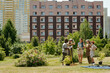 © pressmaster - Group of diverse young adults and teenagers standing together in urban park, holding gardening tools and plants, engaging in community gardening activity with residential buildings behind