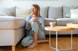 © Dragana Gordic - Thoughtful Woman Sitting on Floor by Comfortable Sofa in Bright Living Room
