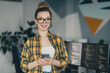 © deagreez - Young female programmer holding smartphone near computer monitors, smiling and working in a modern office environment