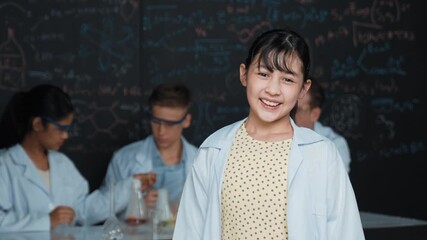 Poster - Cute asian scientist smile to camera while diverse group doing experiment. Young happy schoolgirl standing at blackboard with chemical theory written while wearing lab coat at laboratory. Edification