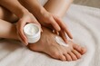 © Татьяна Евдокимова - Close up of hands applying moisturizing cream to a foot, highlighting a self care ritual on a soft towel for healthy skin