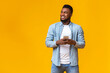 © Prostock-studio - Handsome black man holding smartphone and looking aside at copy space on yellow studio background