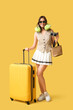 © Pixel-Shot - Happy young woman with packed suitcase, travel pillow and camera on yellow background