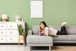 © Pixel-Shot - Young Asian woman talking by mobile phone on grey sofa at home