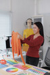© crizzystudio - Fashion designer holding orange sweater and comparing color palette in creative office