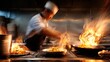 © Nattapol - Mid-action shot of chef flipping food in a hot pan with flames and motion blur