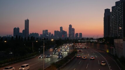 Wall Mural - Traffic moves along the Gangbyeonbuk-ro expressway in Seoul during the twilight hour, with the iconic 63 Building and Yeouido skyline silhouetted against the post-sunset sky.