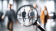 © Almarkha9 - A magnifying glass focuses on blurred figures in a busy office setting, suggesting a search or investigation theme