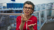 © Krakenimages.com - Senior woman with grey hair gestures for money aboard a boat at sea, wearing a red shirt and glasses against a blurred nautical background, indicating a request for financial help outdoors.