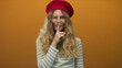 © Krakenimages.com - Woman presses finger shushing in a studio featuring blonde model wearing beret and glasses highlighting lips and smile against orange background.