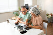 © Fahng - Happy senior couple using laptop counting taxes refund receipts to save money at home. Old man and woman paying bills online planning financial budget savings calculating payment at desk.