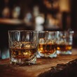 © NatthaphonSiri - Golden Hour Pour Three Glasses of Whiskey with Ice Cubes on a Rustic Bar.